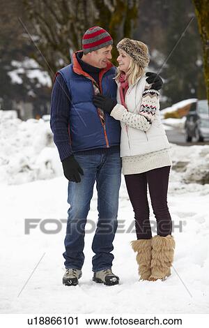 Stock Image - Couple Walking Along Snowy Street In Ski Resort. Fotosearch