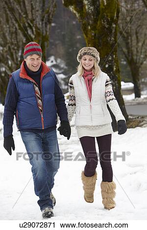 Stock Image - Couple Walking Along Snowy Street In Ski Resort. Fotosearch