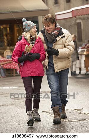 Stock Photo - Couple Walking Along Snowy Town Street In Ski Resort. Fotosearch