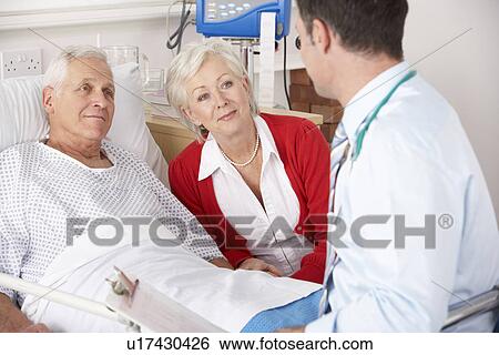 Stock Photograph - Doctor talking to senior couple on UK Hospital ward. Fotosearch