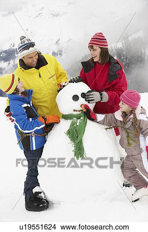 Picture - Family Building Snowman On Ski Holiday In Mountains. Fotosearch