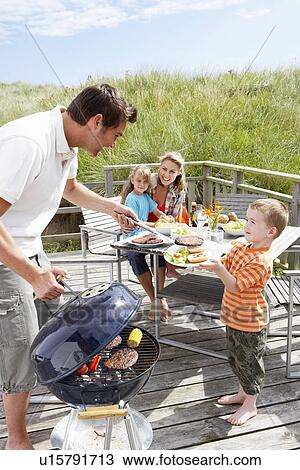 Stock Image - Family on vacation having barbecue. Fotosearch