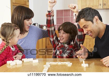 Stock Image - Family Playing Dominoes In Kitchen. Fotosearch