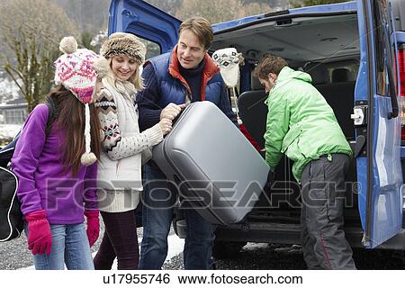 Stock Photograph - Family Unloading Luggage From Transfer Van Outside Chalet On Ski Holiday. Fotosearch