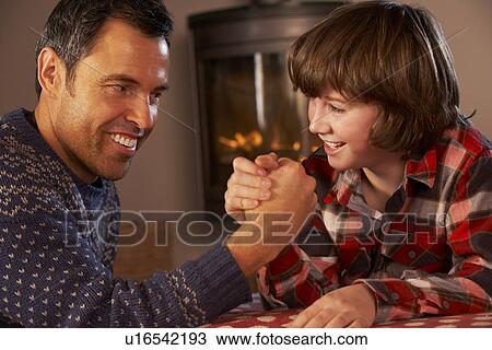 Stock Image - Father And Son Arm Wrestling By Cosy Log Fire. Fotosearch