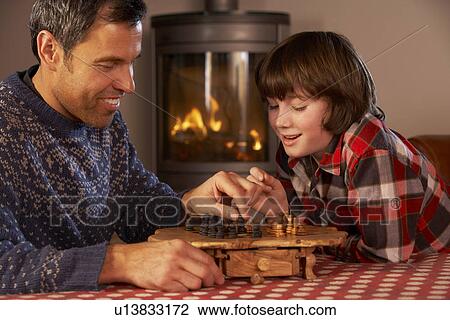 Stock Image - Father And Son Playing Chess By Cosy Log Fire. Fotosearch