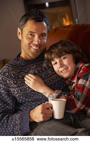 Father And Son Relaxing With Hot Drink Watching TV By Cosy Log Fire View Large Photo Image Stock Photo - Father And Son Relaxing With Hot Drink Watching TV By Cosy Log Fire. Fotosearch
