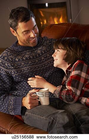 Stock Photo - Father And Son Relaxing With Hot Drink By Cosy Log Fire. Fotosearch