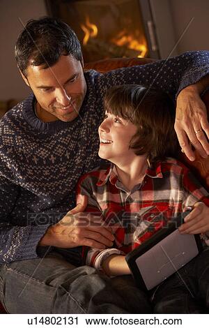 Stock Image - Father And Son Using Tablet Computer By Cosy Log Fire. Fotosearch