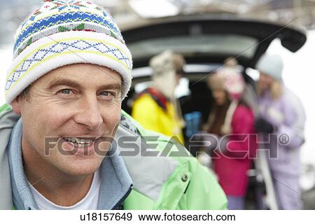 Stock Photo - Father Smiling At Camera Whilst Family Load Skis In Boot Of Car. Fotosearch