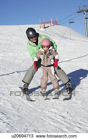 Stock Image - Father Teaching Daughter To Ski Whilst On Holiday In Mountains. Fotosearch