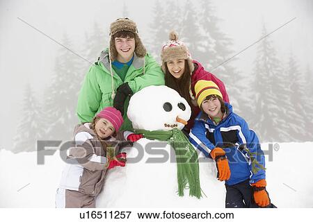 Stock Photo - Group Of Children Building Snowman On Ski Holiday In Mountains. Fotosearch