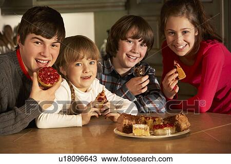 Stock Image - Group Of Children Enjoying Plate Of Cakes In Kitchen. Fotosearch