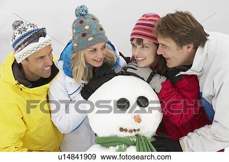 Stock Photo - Group Of Friends Building Snowman On Ski Holiday In Mountains. Fotosearch