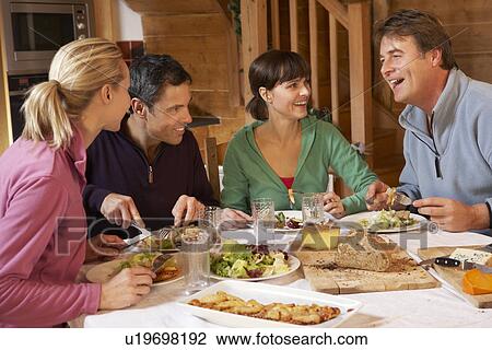 Stock Image - Group Of Friends Enjoying Meal In Alpine Chalet Together. Fotosearch