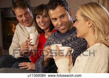 Picture - Group Of Middle Aged Couples Sitting On Sofa With Hot Drinks Talking. Fotosearch