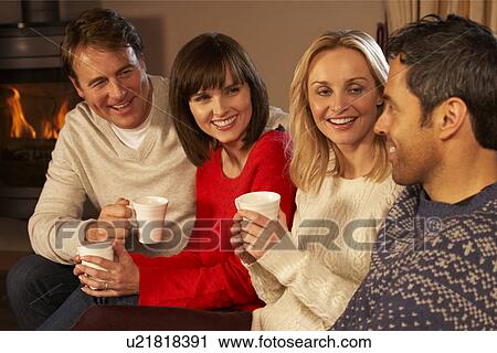 Stock Image - Group Of Middle Aged Couples Sitting On Sofa With Hot Drinks Talking. Fotosearch