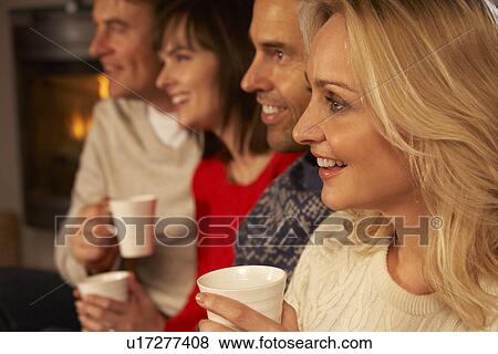 Group Of Middle Aged Couples Sitting On Sofa With Hot Drinks Watching TV View Large Photo Image Stock Photo - Group Of Middle Aged Couples Sitting On Sofa With Hot Drinks Watching TV. Fotosearch