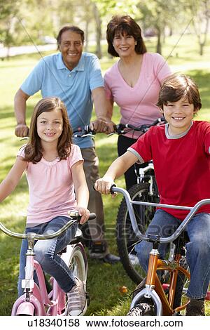 Stock Photo - Hispanic family riding bikes in park. Fotosearch