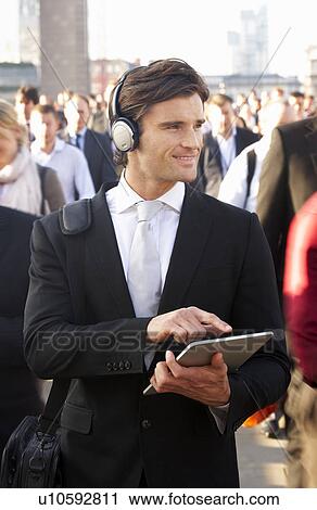 Stock Image - Male commuter in crowd with tablet and headphones. Fotosearch