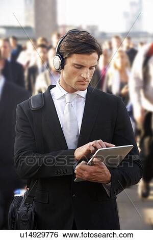 Stock Photograph - Male commuter in crowd with tablet and headphones. Fotosearch