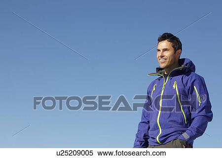 Stock Photography - Man Standing In Snow Wearing Warm Clothes On Ski Holiday In Mountains. Fotosearch