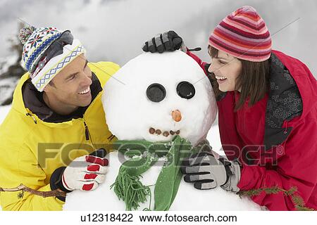 Stock Image - Middle Aged Couple Building Snowman On Ski Holiday In Mountains. Fotosearch