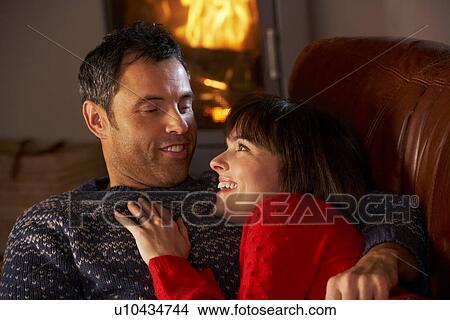 Picture - Middle Aged Couple Chatting On Sofa By Cosy Log Fire. Fotosearch