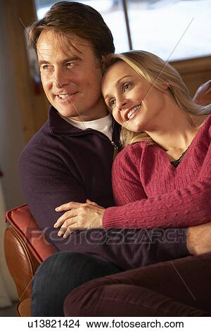 Picture - Middle Aged Couple Chatting On Sofa In Chalet With Winter View. Fotosearch