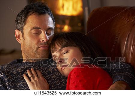 Stock Photography - Middle Aged Couple Cuddling On Sofa By Cosy Log Fire. Fotosearch