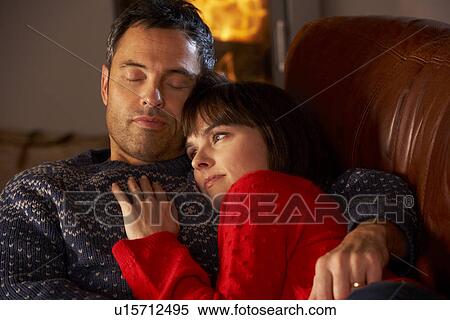 Stock Photography - Middle Aged Couple Cuddling On Sofa By Cosy Log Fire. Fotosearch