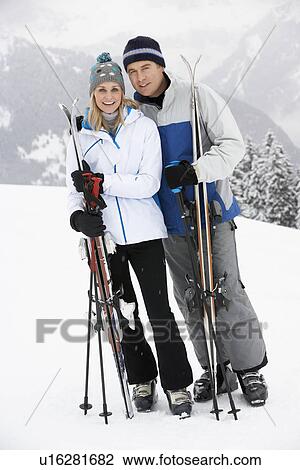 Stock Image - Middle Aged Couple On Ski Holiday In Mountains. Fotosearch