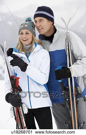 Stock Image - Middle Aged Couple On Ski Holiday In Mountains. Fotosearch