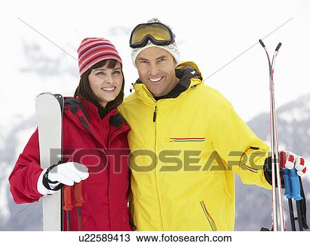 Stock Image - Middle Aged Couple On Ski Holiday In Mountains. Fotosearch