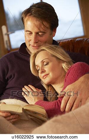 Stock Photography - Middle Aged Couple Relaxing On Sofa In Chalet With Winter View. Fotosearch