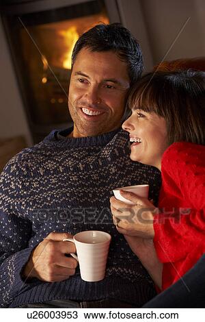 Middle Aged Couple Sitting On Sofa By Cosy Log Fire With Hot Drink View Large Photo Image Stock Image - Middle Aged Couple Sitting On Sofa By Cosy Log Fire With Hot Drink. Fotosearch