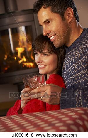 Stock Photo - Middle Aged Couple Sitting On Sofa Watching TV By Cosy Log Fire. Fotosearch