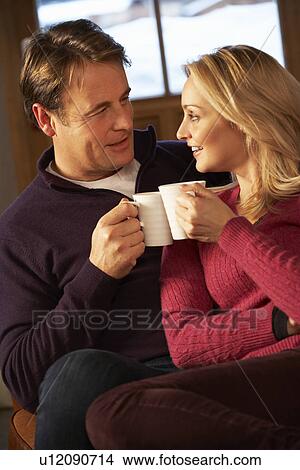 Picture - Middle Aged Couple Sitting On Sofa With Hot Drinks. Fotosearch