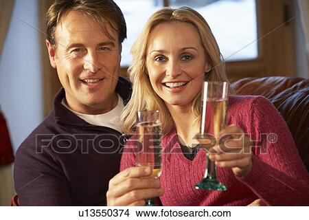 Picture - Middle Aged Couple Sitting On Sofa With Glasses Of Champagne. Fotosearch