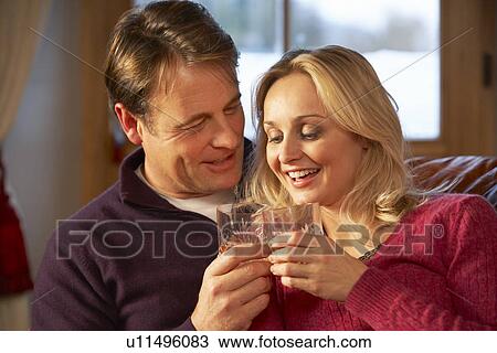Stock Image - Middle Aged Couple Sitting On Sofa With Glasses Of Whisky. Fotosearch
