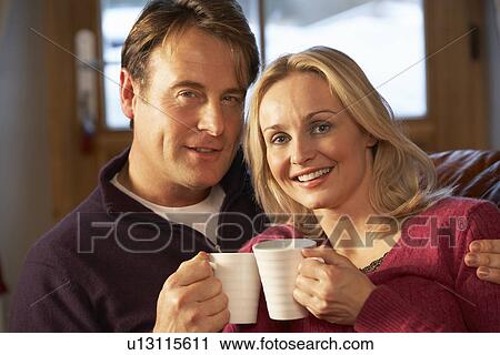 Middle Aged Couple Sitting On Sofa With Hot Drinks View Large Photo Image Stock Image - Middle Aged Couple Sitting On Sofa With Hot Drinks. Fotosearch