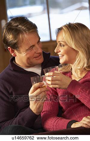 Stock Image - Middle Aged Couple Sitting On Sofa With Glasses Of Whisky. Fotosearch