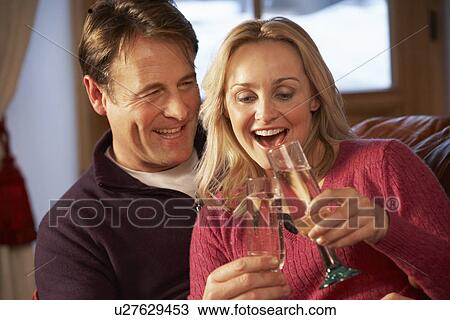 Stock Image - Middle Aged Couple Sitting On Sofa With Glasses Of Champagne. Fotosearch