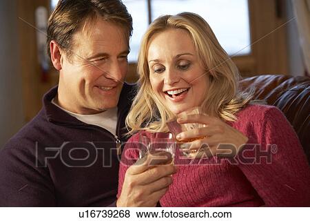 Stock Photo - Middle Aged Couple Sitting On Sofa With Glasses Of Whisky. Fotosearch