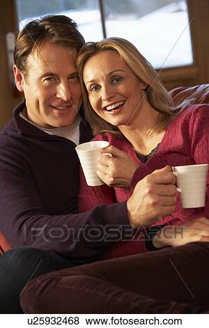 Stock Photo - Middle Aged Couple Sitting On Sofa With Hot Drinks. Fotosearch