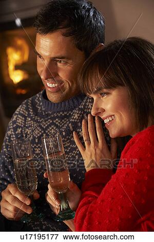 Stock Photo - Middle Aged Couple Sitting Sofa By Cosy Log Fire With Glass Of Champagne. Fotosearch
