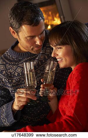 Stock Photo - Middle Aged Couple Sitting Sofa By Cosy Log Fire With Glass Of Champagne. Fotosearch