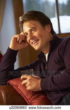 Stock Image - Middle Aged Man Relaxing Sitting On Sofa Drinking Whisky. Fotosearch