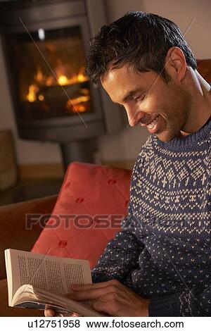 Stock Photo - Middle Aged Man Relaxing With Book By Cosy Log Fire. Fotosearch