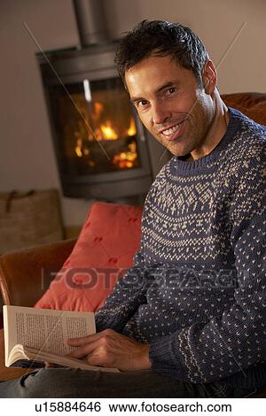 Stock Photograph - Middle Aged Man Relaxing With Book By Cosy Log Fire. Fotosearch